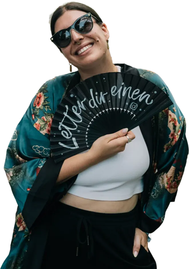 Lächelnde Frau mit Sonnenbrille hinter einem schwarzen Handfächer mit dem Schriftzug „Letter dir einen“